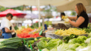 Fresh vegetables on display at a Colorado farmers market, with local vendors and shoppers in the background under sunlit tents.