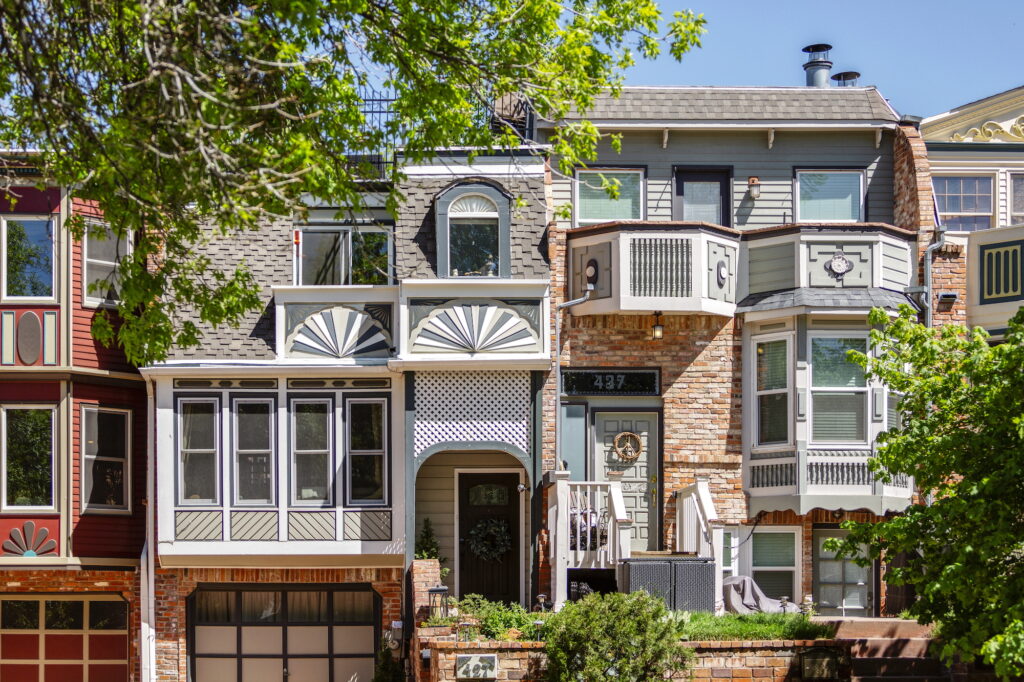 Row of colorful historic-style townhomes in Boulder’s Mapleton Hill neighborhood, featuring brick facades, bay windows, and detailed trim surrounded by leafy trees.