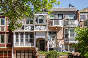 Row of colorful historic-style townhomes in Boulder’s Mapleton Hill neighborhood, featuring brick facades, bay windows, and detailed trim surrounded by leafy trees.