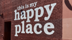 White block letters painted on a red brick wall read “this is my happy place,” part of a mural in Downtown Boulder on the Pearl Street Mall.